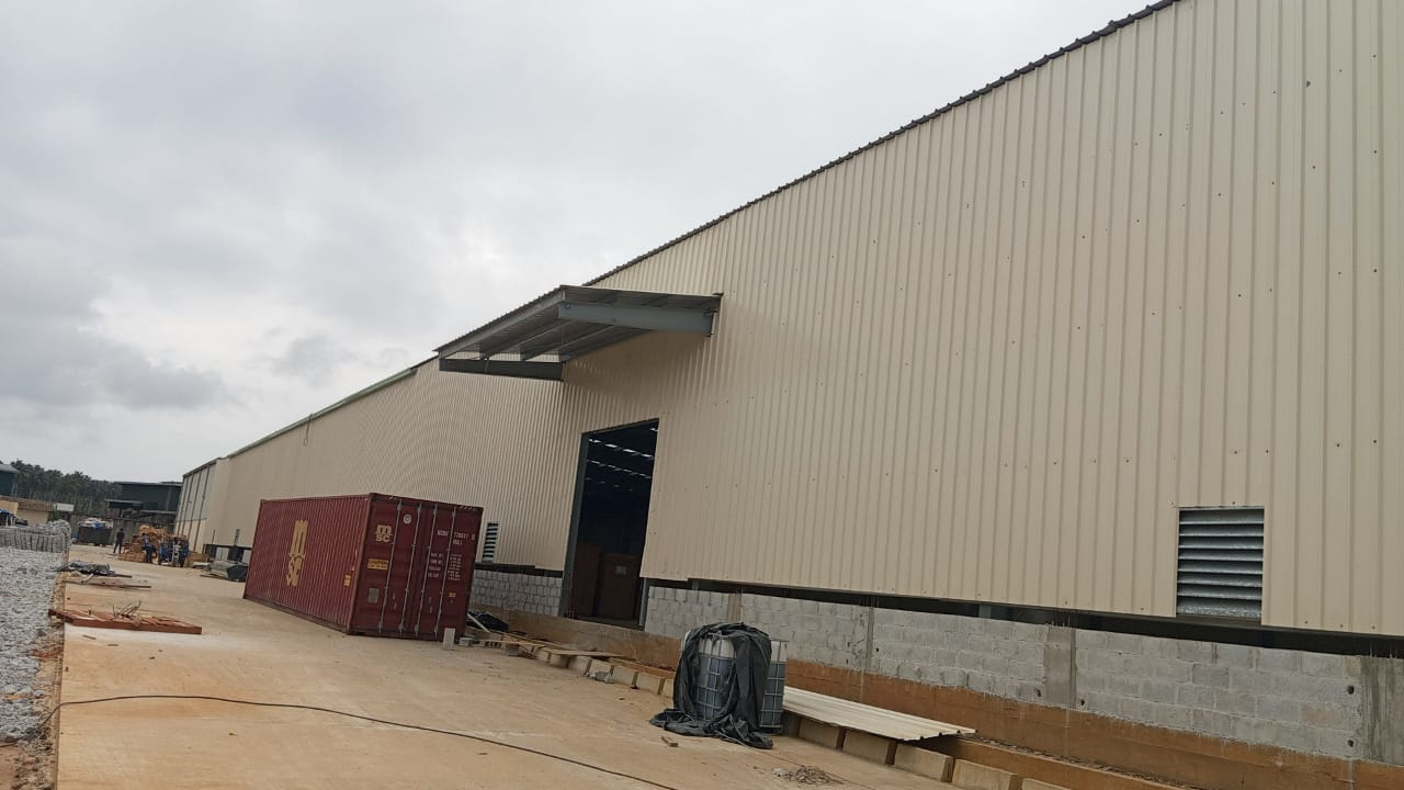 Charpente industrielle agroalimentaire 5 001 m² à Bonoua : bardage beige, structure métallique, couverture et montage en cours — vue 2