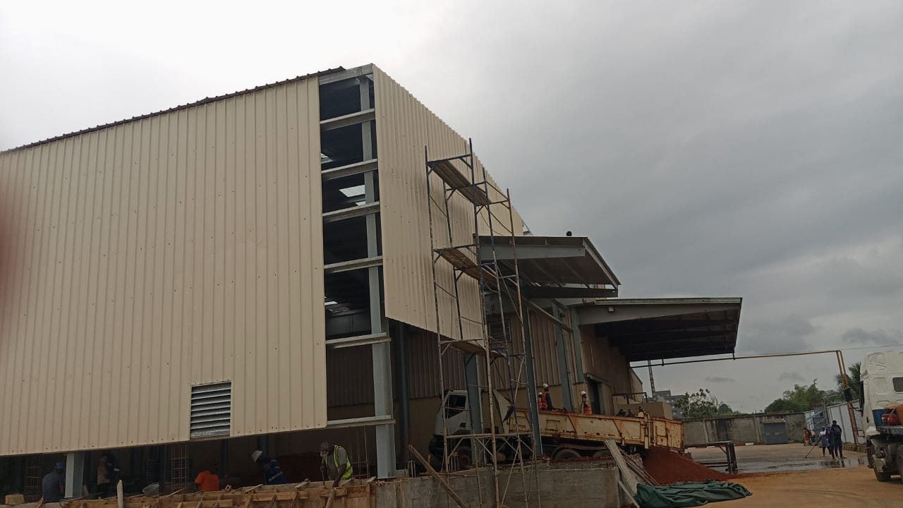 Charpente industrielle agroalimentaire 5 001 m² à Bonoua : bardage beige, structure métallique, couverture et montage en cours — vue 1